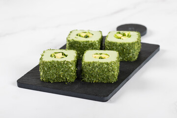 Sushi avocado, square rolls with finely chopped greens on a serving board on a white background