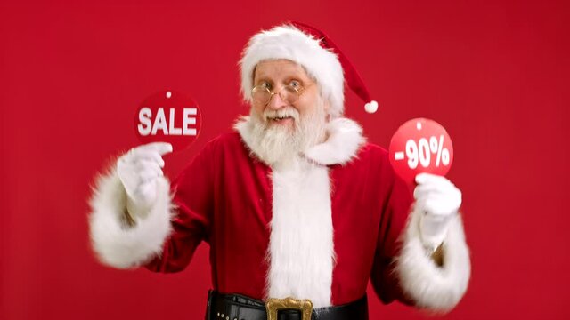 Christmas SALE -90 Off. Cheerful Santa Claus is Dancing and Joyful From Christmas Sale Holding Two Banners With Inscription SALE and -90 Off Showing Off Inscriptions to Camera on Red Background.