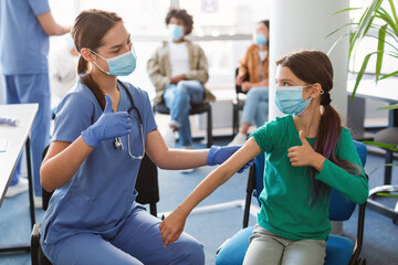 Vaccinated Girl And Nurse Gesturing Thumbs Up At Clinic