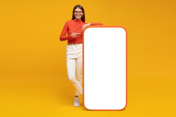 Young woman standing and showing with finger blank screen of huge phone, mockup for your app - obrazy, fototapety, plakaty