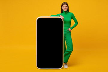 Happy young woman standing and showing blank screen of huge phone, mock up for your app