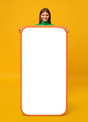Happy young woman standing behind blank screen of huge phone, mockup for your app