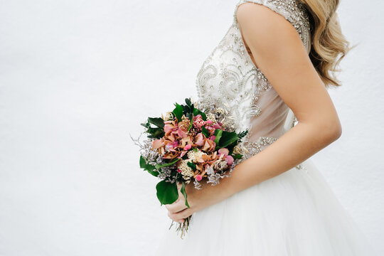 Crop anonymous bride with bouquet near wall