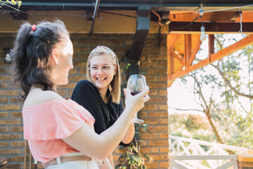 Delighted teenage ladies toasting with wine and smiling on terrace
