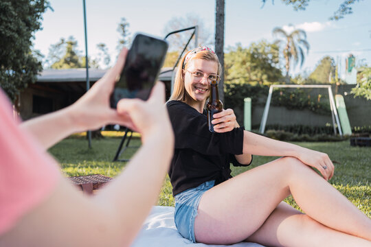 Unrecognizable lady taking photo of cheerful female friend in park