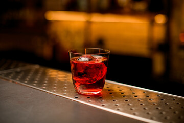transparent glass of cocktail with piece of ice stands on a bar counter