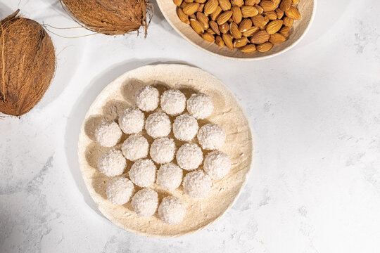 Sweet coconut candies in round plate, coconuts and almond nuts on background, banner with free space