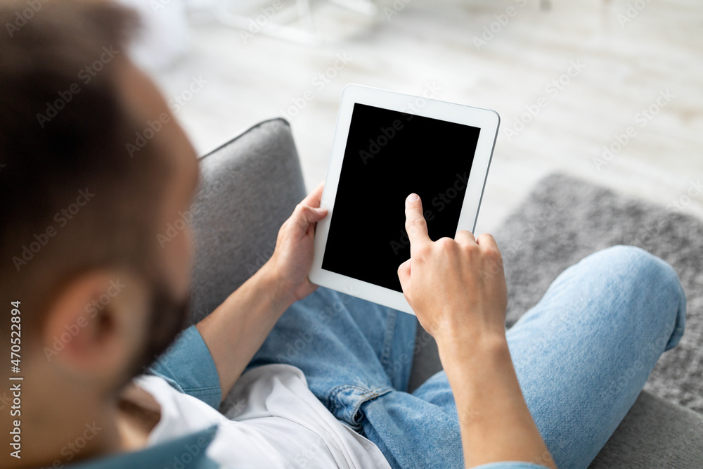 Poster Millennial man using tablet computer with blank black screen, browsing website or demonstrating new app at home