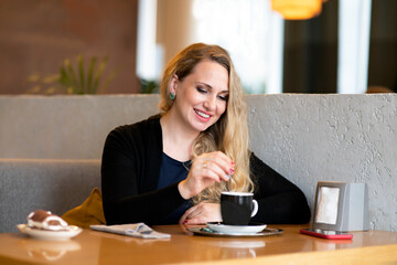 Young woman in a coffee shop drinks coffee, in a shop. Happy female smiling and stirring cappuccino...