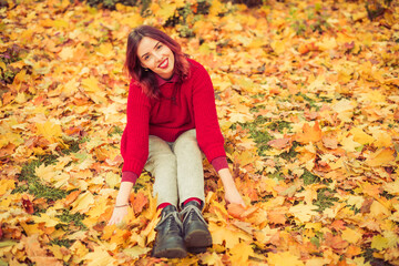 Obraz na płótnie Canvas young happy woman in red sweater sitting in colorful autumn leafs