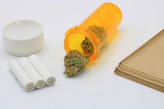 Marijuana buds in an orange pot accompanied by smoke paper and insulated filters on a white background