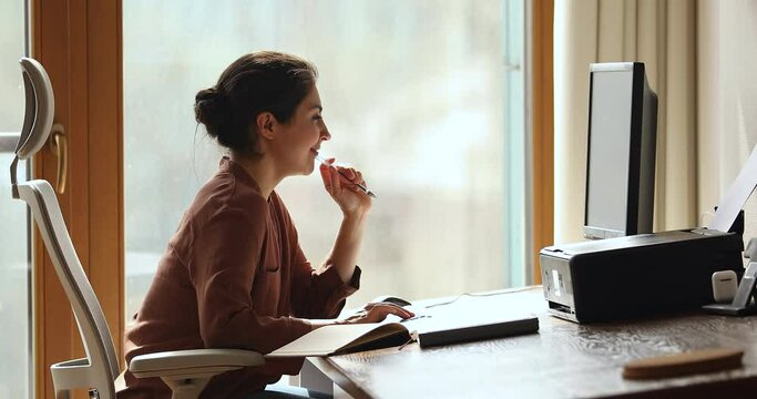 Focused young Indian woman sit in comfy office chair watch webinar coaching in internet answer electronic test questions using desktop computer. Millennial female remote worker engaged in online job