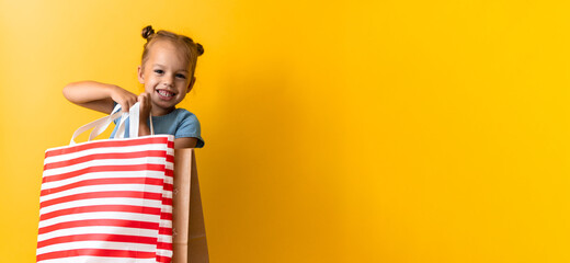 Banner Portrait Caucasian Beautiful Happy Little Preschool Girl Smiling Cheerful And Holding Cardboard Bags Isolated On Orange Yellow Background. Happiness, Consumerism, Sale People shopping Concept