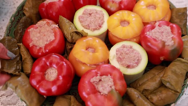 People hands are preparing food. Peppers, tomatoes, zucchini and grape leaves stuffed with minced meat.