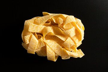 uncooked dried pappardelle pasta on black background