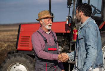 Farmers shaking hands in front of tractor in field