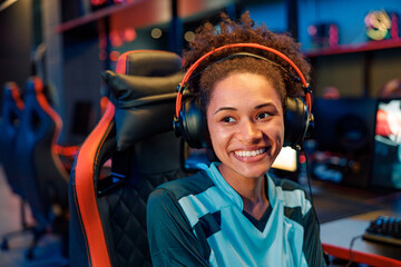 Young cute African woman esports gamer wearing wired headphones sitting on streaming chair and...