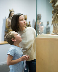 Young woman with son observing with interest sculptures exhibition in art museum, pointing to...