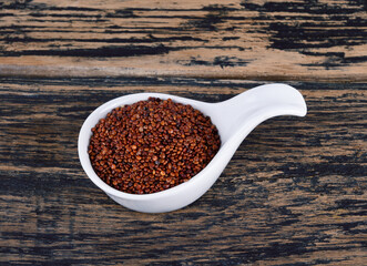 Red quinoa grains in white spoon bowl isolated on wooden background