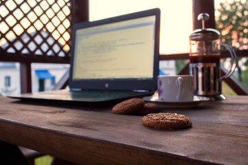 Laptop with code on the screen, cup of coffee, cookies, french press, lies on the table in the...