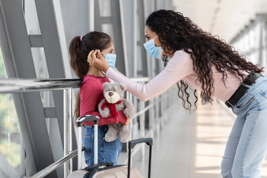 Loving Mom Adjusting Protective Medical Mask On Little Daughter's Face In Airport