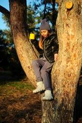 A girl in a purple suit and hat walks through the woods and drinks tea. Travel concept with children. Autumn forest.