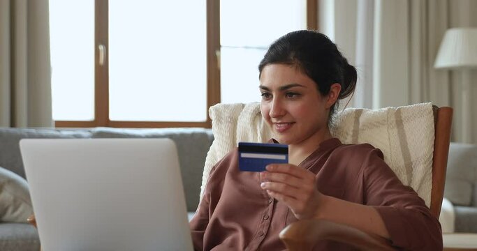Happy young female internet bank customer succeeded in paying online from home in web app on laptop. Millennial Indian lady make easy safe transaction cashless payment on pc using personal credit card