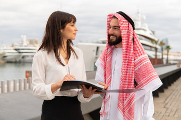 Young friendly europian businesswoman explaning contract details to arab man during meeting in port