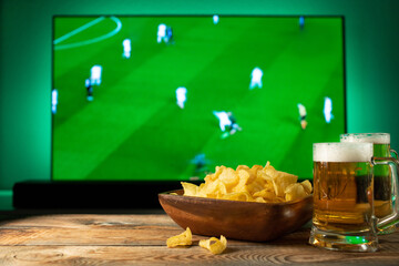 Beer and snacks set on football match tv background