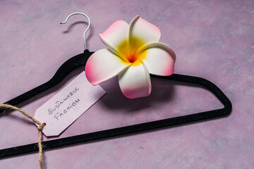 environmentally conscious clothing brands, Sustainable Fashion label with clothes hanger on pink background with tropical frangipani flower