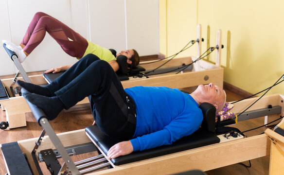 Portrait of elderly man performing set of pilates exercises on reformer during group workout. Active lifestyle and wellness concept of seniors