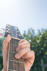 Selective focus of a hand holding an acoustic guitar outdoors, with the sky and greenery in the background