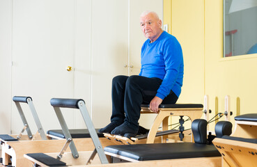 Portrait of elderly man doing remedial gymnastics on pilates combo chair. Health and wellness of seniors concept