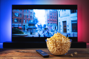 A glass bowl of popcorn and remote control in the background the TV works. Evening cozy watching a...