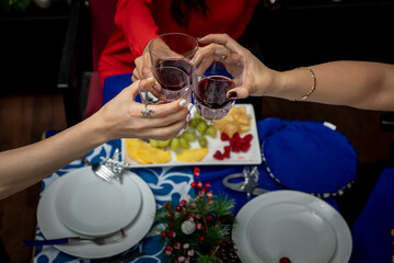 Obraz na płótnie Canvas top view of hands with glasses toasting at a christmas dinner, with christmas decoration in the background