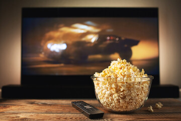A glass bowl of popcorn and remote control in the background the TV works. Evening cozy watching a...