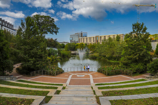 a gorgeous shot of the green lake with water fountain in the center of the water, green and autumn colored trees with African American people standing near the lake at Historic Fourth Ward Park