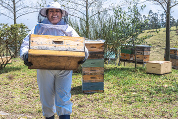 Portrait of a female beekeeper in protective suit carrying a crate of honeycomb with honey in the...