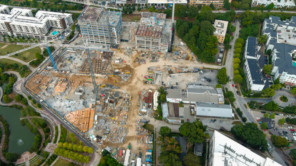 a stunning aerial shot of tower cranes on dirt covered a construction site surrounded by buildings...