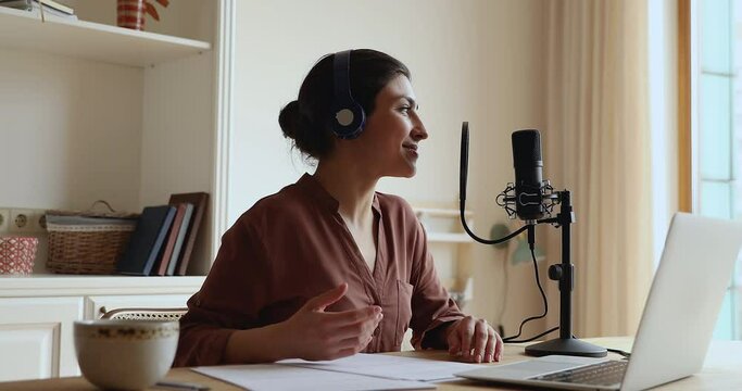 Indian lady in headset talk make podcast for social media using microphone with pop filter fixed in shock mount and pc app. Young woman do professional video voiceover at home audio recording studio