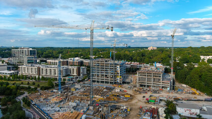 a stunning shot of tall tower cranes on dirt covered a construction site surrounded by buildings...