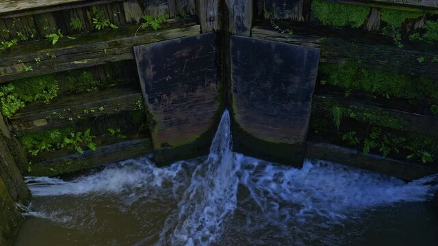 Canal lock with water pouring throuigh large wooden gates into old barge narrowboat lift system.