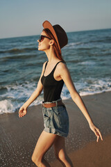 Fototapeta na wymiar cheerful woman in sunglasses and a hat walks along the ocean
