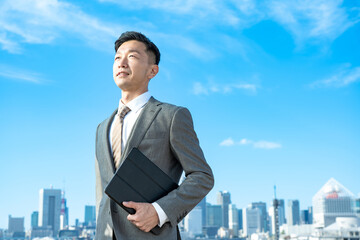 青空とビル群を背景にしたビジネスマンのポートレート