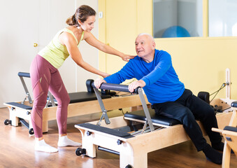 Elderly man doing exercise with her personal trainer in pilates studio