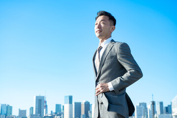 Fototapeta premium 青空とビル群を背景にしたビジネスマンのポートレート