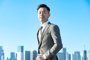 青空とビル群を背景にしたビジネスマンのポートレート