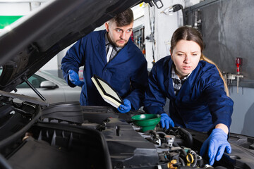 Man and woman masters replacing oil in the car at workplace.