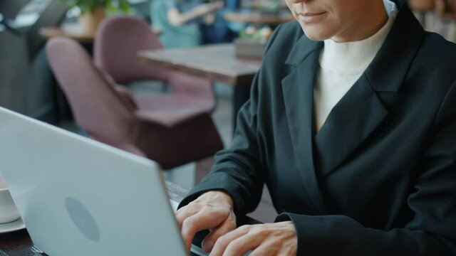Slow motion portrait of elegant girl working typing with laptop and drinking coffee in nice cafe. Freelance work and contemporary devices concept.