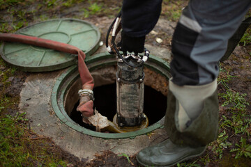 Sewer repair. The worker lowers the equipment into the sewer hatch. - obrazy, fototapety, plakaty